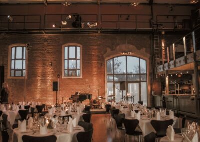 Festlich gedeckte Eventlocation mit Backsteinwänden und Bühne für Catering in Hannover